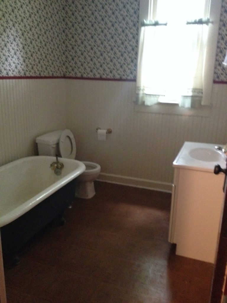 Queen Anne bathroom before renovation. It has beadboard and wallpaper walls and a clawfoot tub.