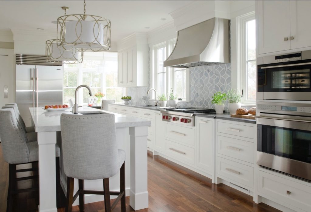 Modern kitchen design: white cabinets with sleek silver hardware, an island with bar stools, and two ovens.