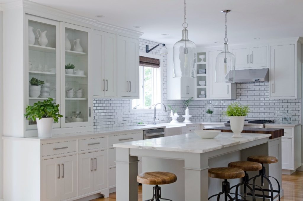 Modern kitchen design: white cabinets with sleek silver hardware, an island with bar stools and granite countertop, and glass pendant lights.